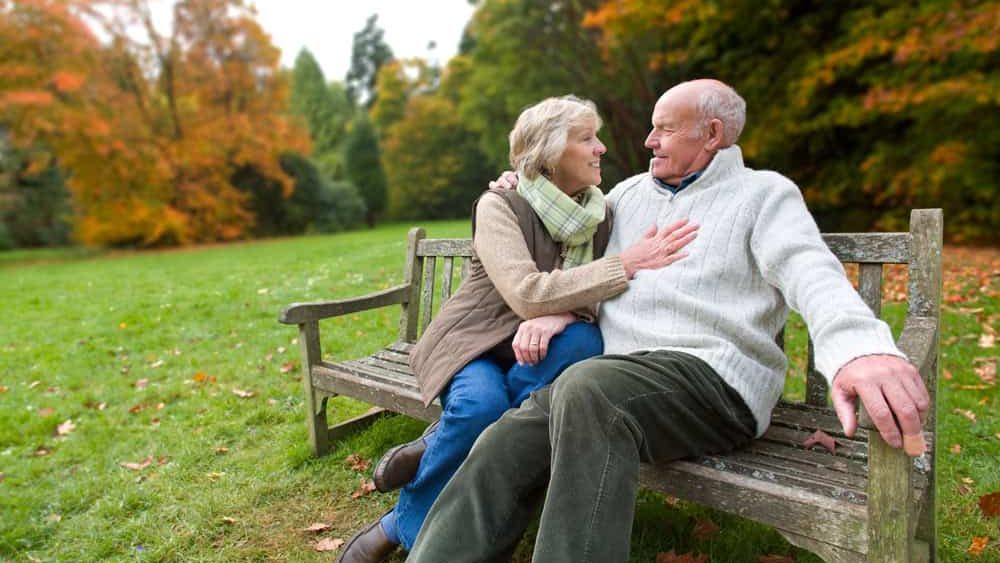 Elderly gray-haired couple sitting on the bench on an autumn day.