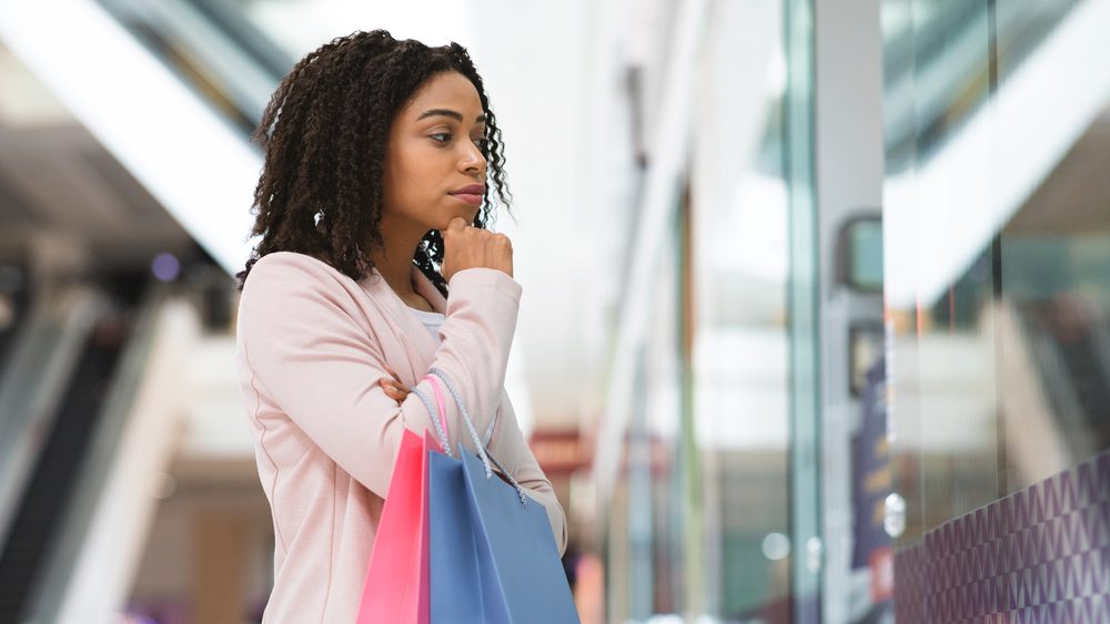 Pensive black shopaholic woman looking at showcase in department store, choosing new fashion clothes, thoughtful african woman doing shopping in modern mall, thinking about interesting discount offer
