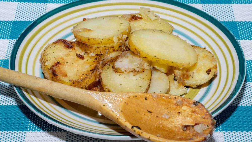 Hot baked potato slices with thin skinned potatoes on a plate with a wooden spoon. A simple and quick after-work meal for the worker and bachelor. Inexpensive food for poor people and farmers
