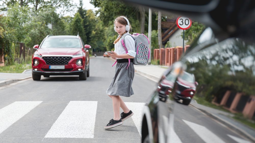 Scared girl with phone and headphones runs away from the car at a pedestrian crossing