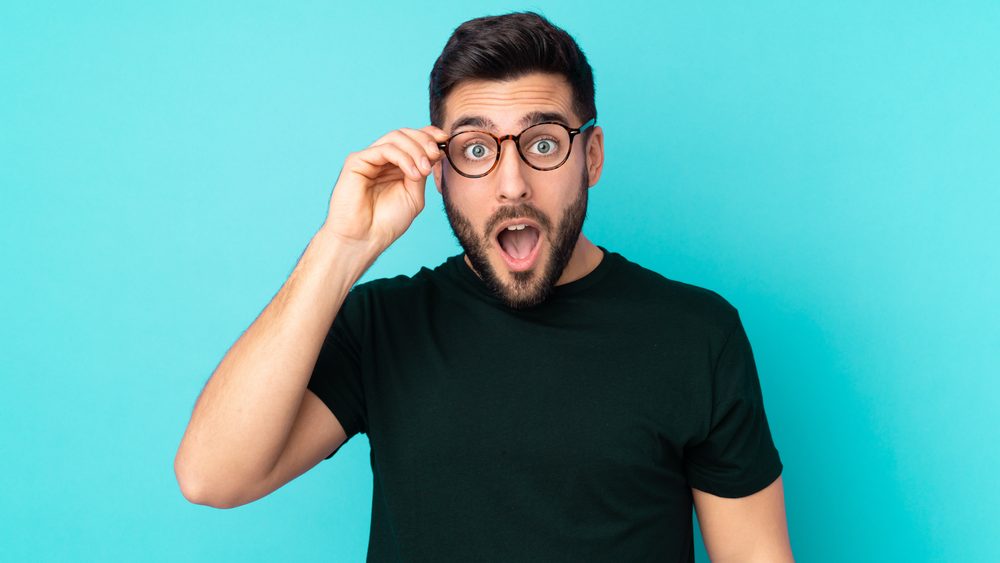 Caucasian handsome man isolated on blue background with glasses and surprised