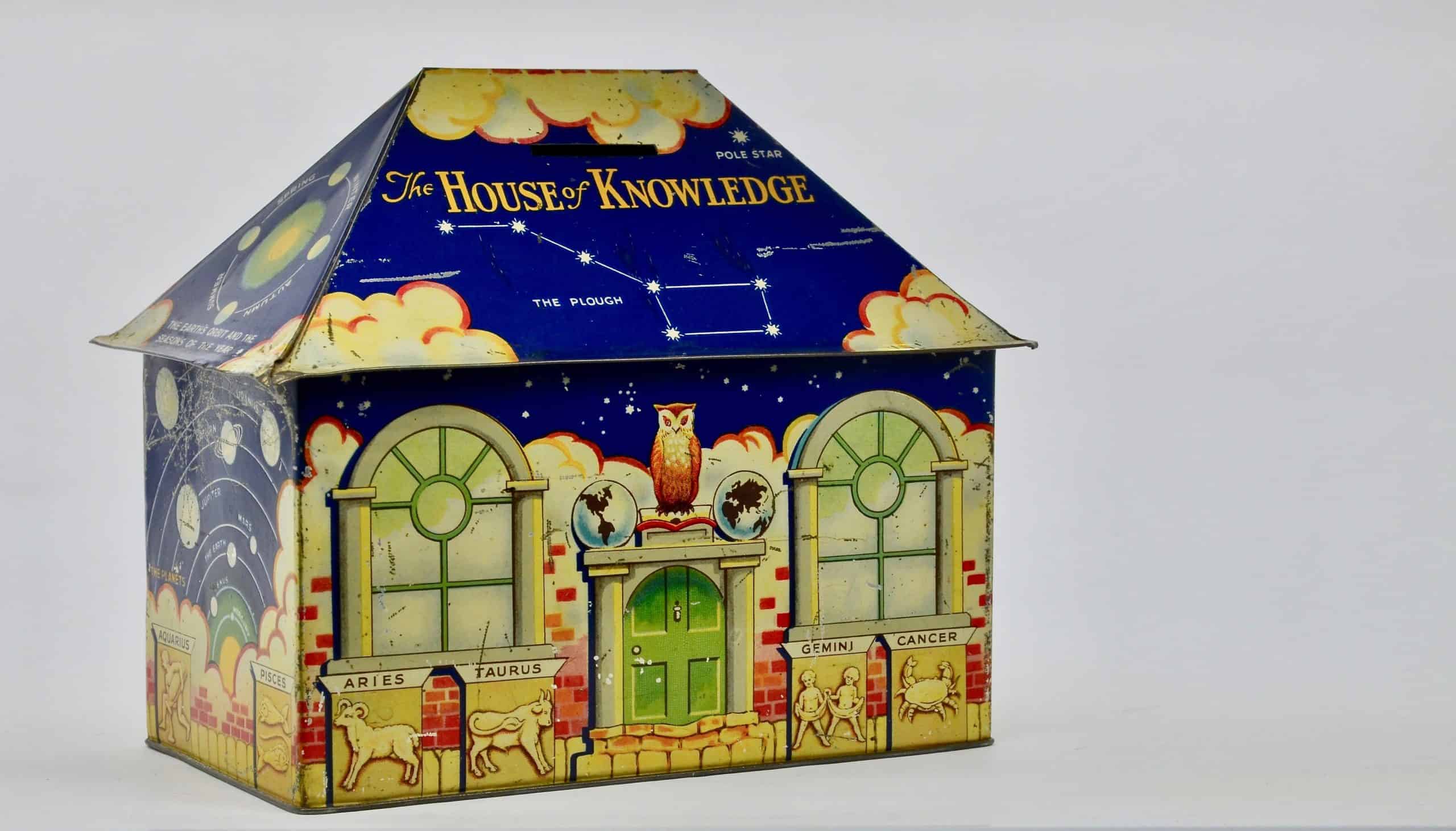 LONDON - APRIL 14, 2021. A vintage litho printed tinplate biscuit tin money box House of Knowledge on plain background c1939, London, UK.