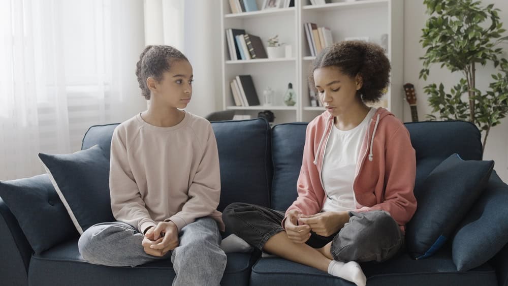 Black teenage girl telling bad news to best friend at home, sharing a secret