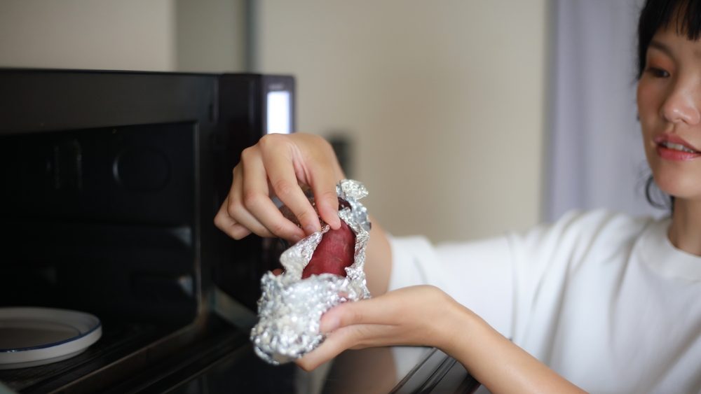 A woman who wraps sweet potatoes in aluminum foil and tries to heat them in the microwave
