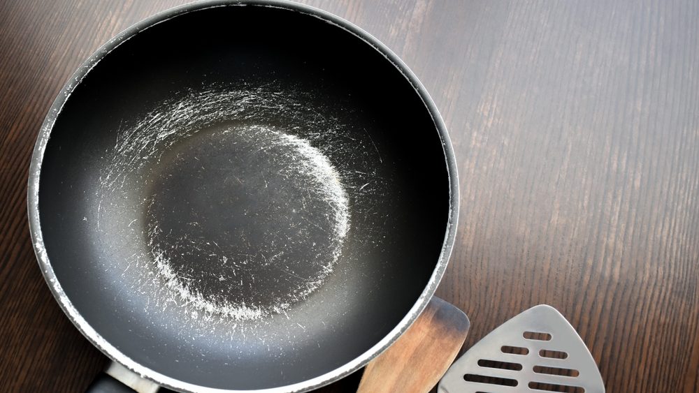 Old scratched non-stick pan on wood table. Pan peeling off. Copy space is on the right side.