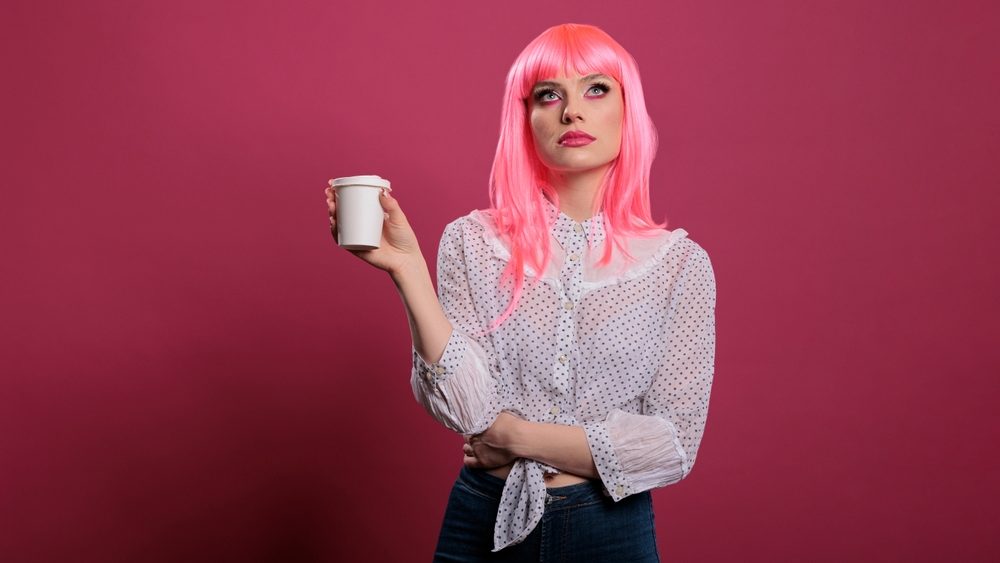 Caucasian woman doing eye roll gesture and holding cup of coffee, feeling displeased and indifferent in front of camera. Having annoyed attitude and feeling discontent, uninterested.