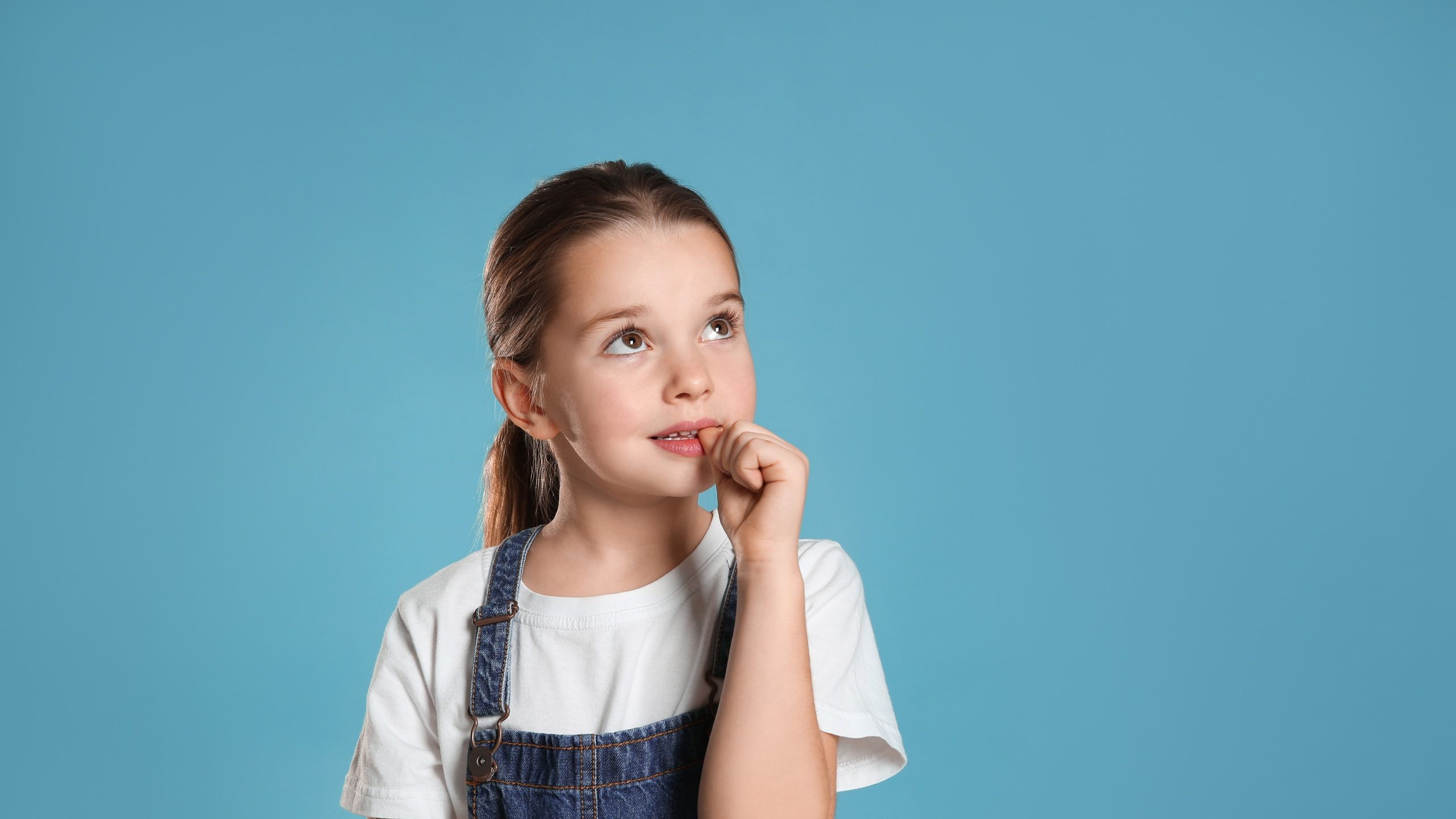 Cute little girl biting her nails on turquoise background, space for text