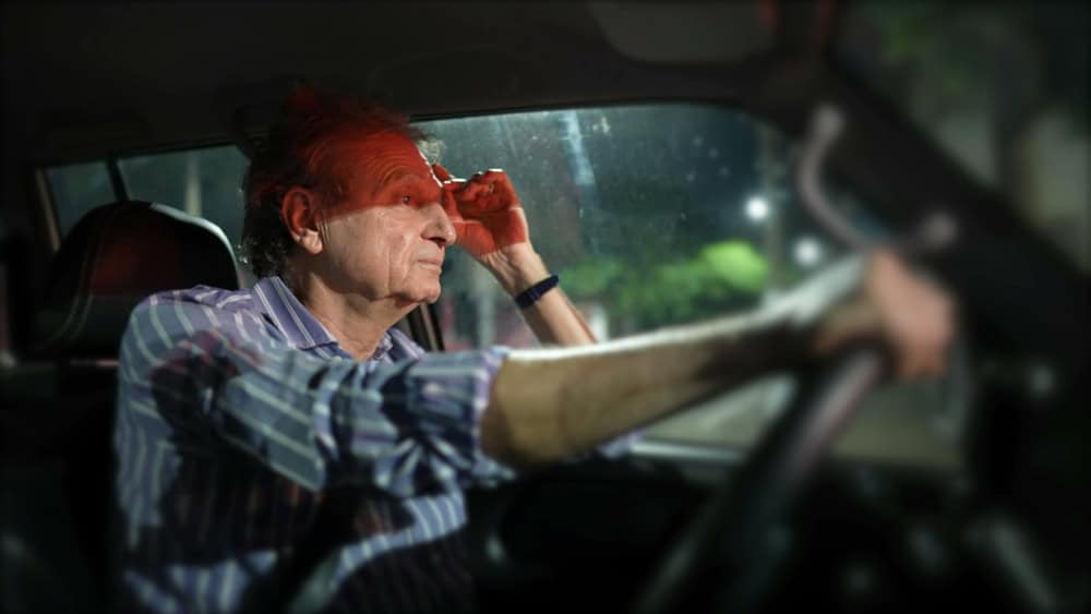 Pensive older man waiting in red light at night holding car steering wheel. Thoughtful senior person waits in signal