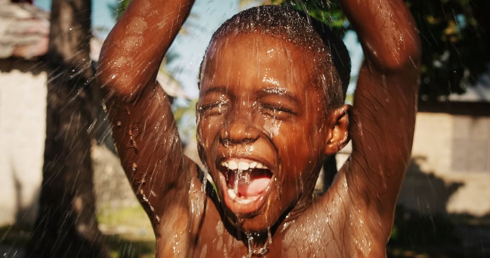 Portrait of an African Little Boy Jumping and Dancing Under Pouring Water. Happy and Innocent Black Children Playing and Enjoying the Blessing of Rain Water After Long Drought and a Hot Weather