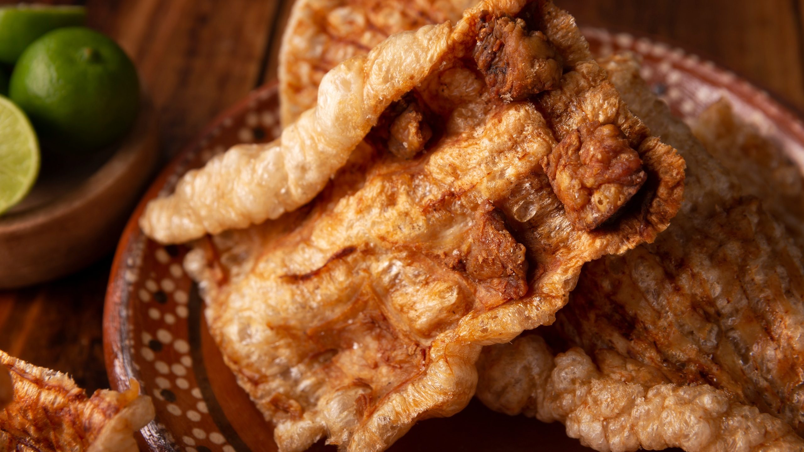 Chicharron. Crispy Fried pork rind, are pieces of aired and fried pork skin, traditional Mexican ingredient or snack served with lime juice and red hot sauce. Closeup.