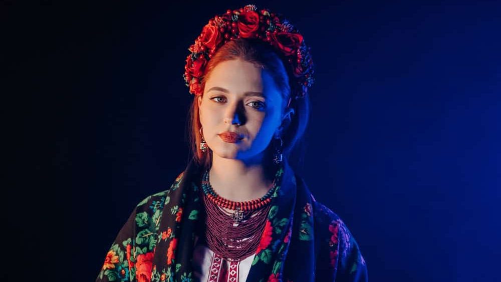 Charming ginger woman in traditional ukrainian handkerchief, necklace and embroidered blouse at black background. Ukraine, style, folk, ethnic culture. High quality photo