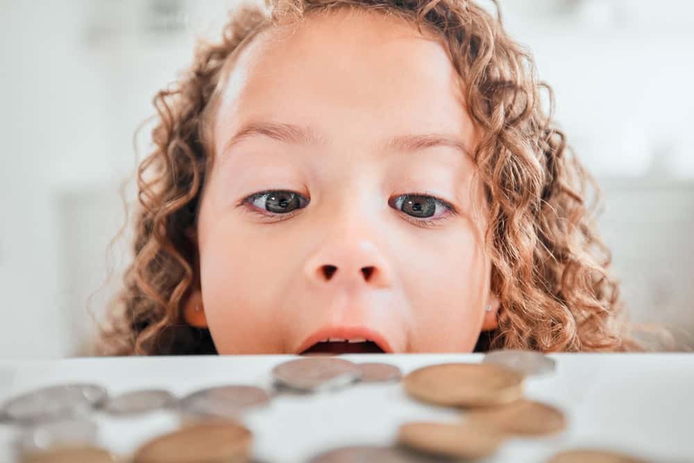 Finance, surprise and coins with child at home for savings, money and budget. Growth, learning and cash with face of shocked girl and change on table for investment, profit or banking responsibility