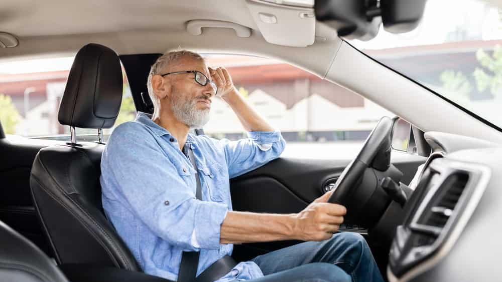 Senior man driving car despair after accident. Upset driver, stressful situations on road, fast rhythm in modern city. Unhappy tired pensioner holding steering wheel in auto, presses hand to his head
