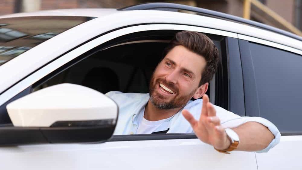 Happy bearded man looking out of car window on city street, view from outside. Enjoying trip
