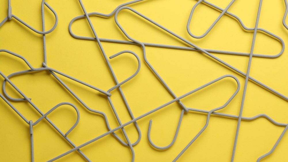 Empty hangers on yellow background, top view