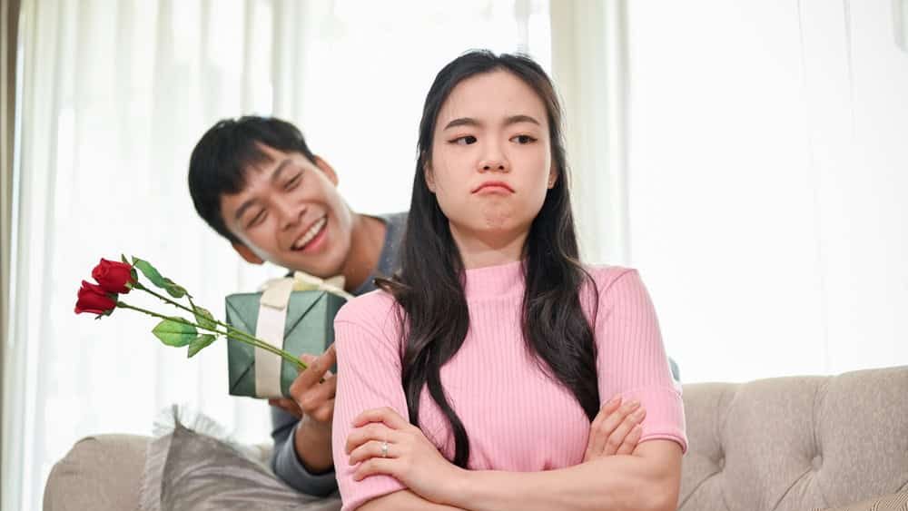 A romantic Asian husband is trying to ask for forgiveness from his angry wife by surprising her with a present and flowers in the living room. family bonding, love and care couple