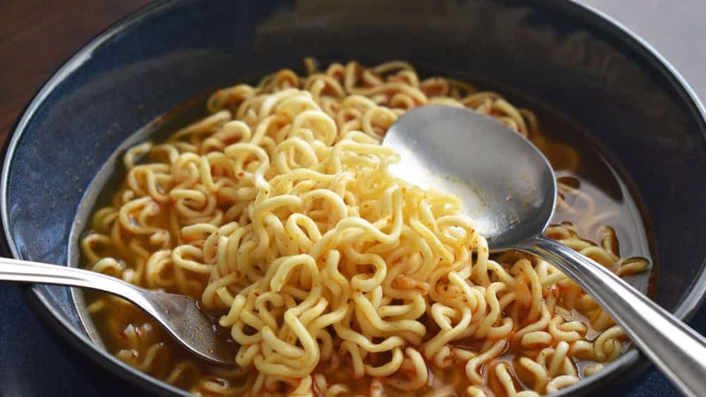 Instant noodles in a bowl with a spoon and a fork. Eating noodle soup. Homemade speed food. Asian dishes.