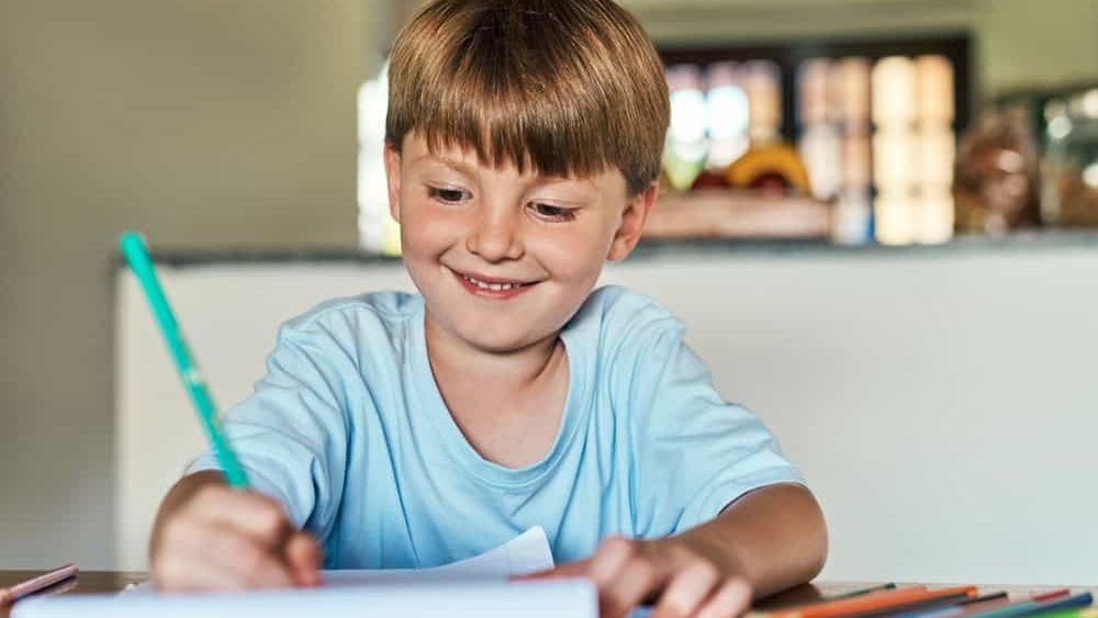 Learning, writing and boy with homework, education and creative assignment for child development with smile. House, student and book to practice handwriting, spelling and grammar with art project