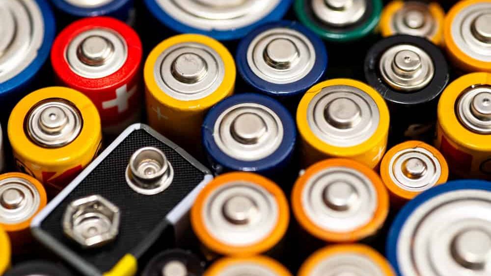 Background made of various alkaline and lithium-ion batteries, positive pole visible.