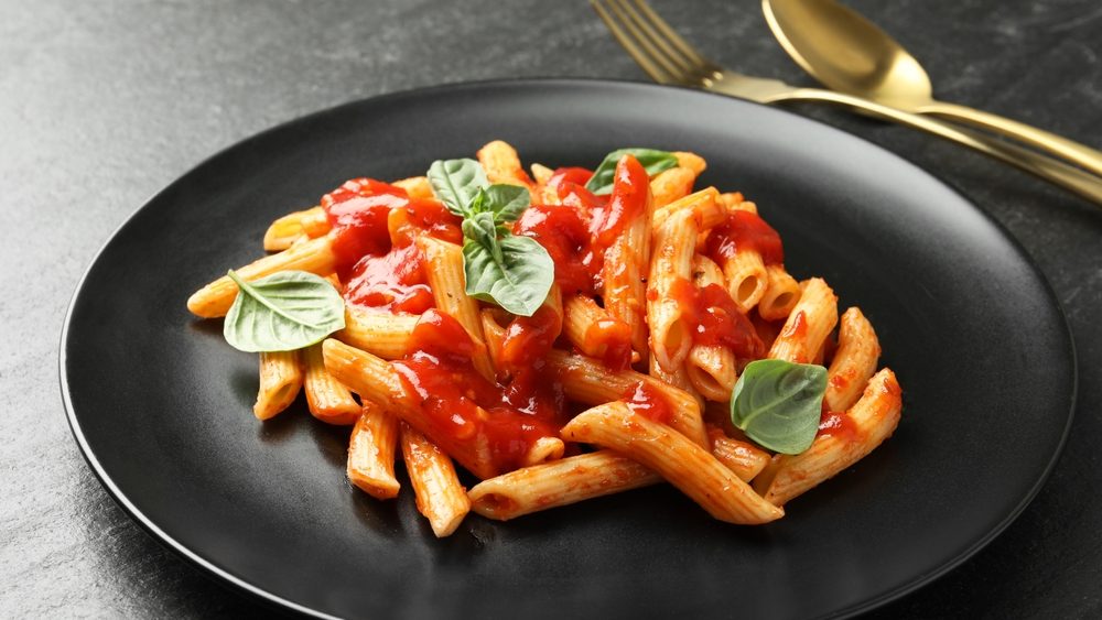Delicious pasta with tomato sauce and basil served on black textured table, closeup