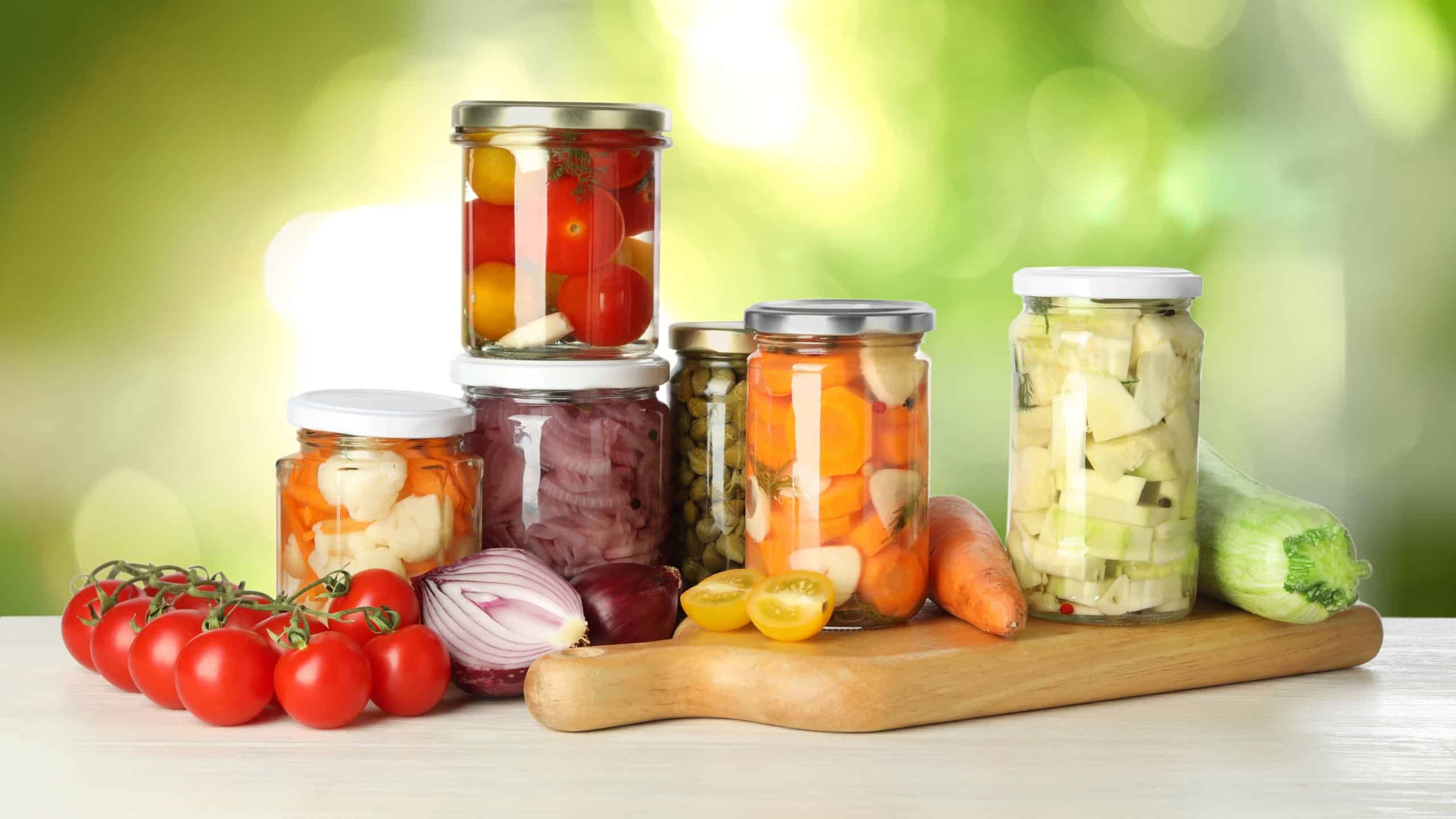 Jars with pickled vegetables on white wooden table outdoors