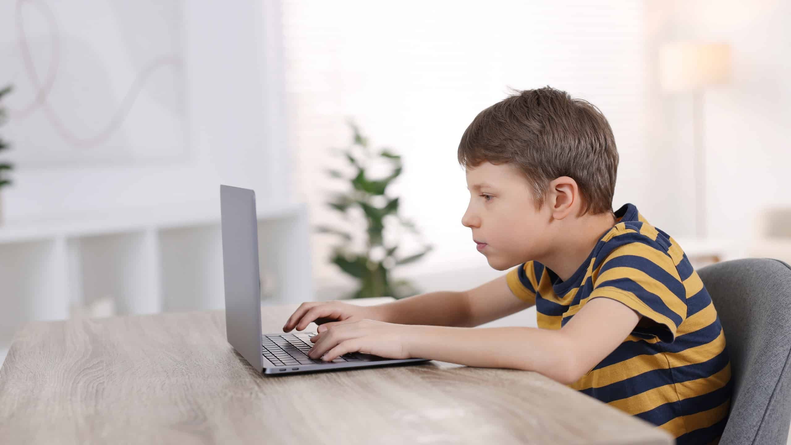 Boy with incorrect posture using laptop at wooden desk indoors
