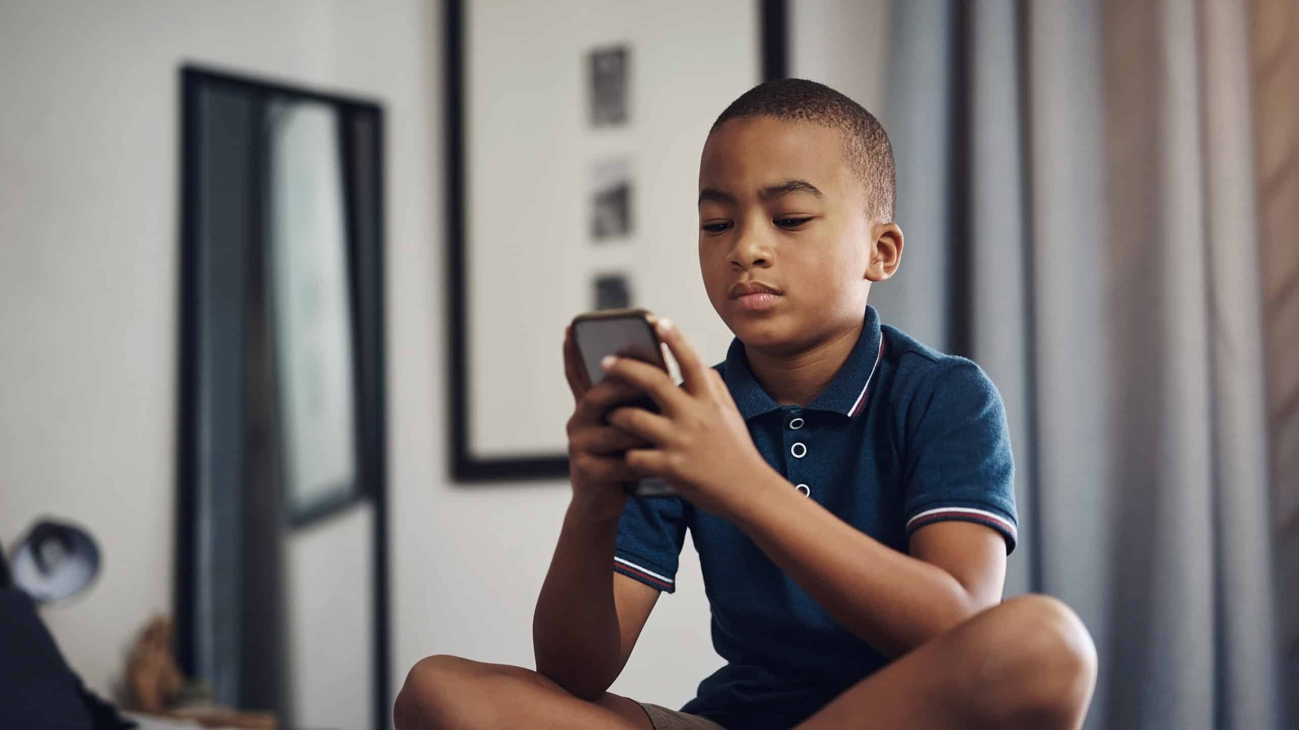 Games, serious and child with smartphone, bedroom and concentration for score, playing and fun in home and online. Bed, digital and boy with mobile for app and browsing for entertainment and house