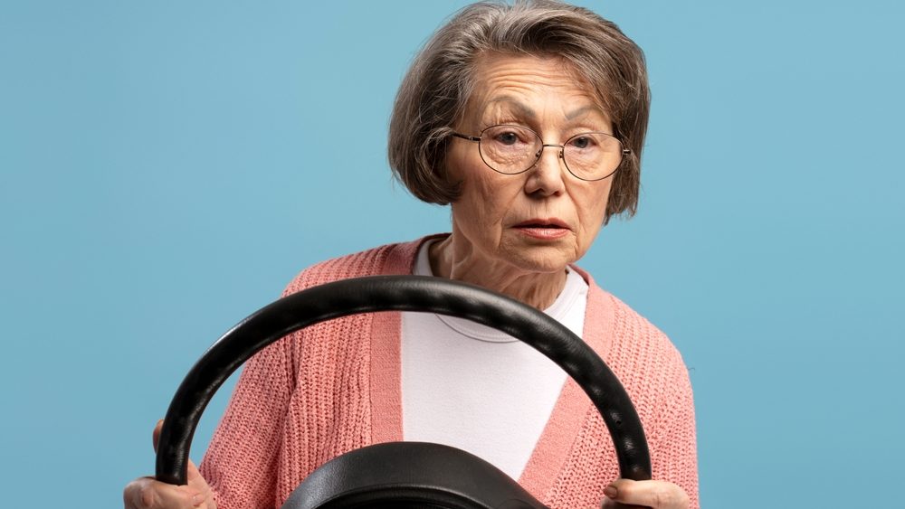 Concentrated senior woman driving car holding steering wheel and looking away on blue background