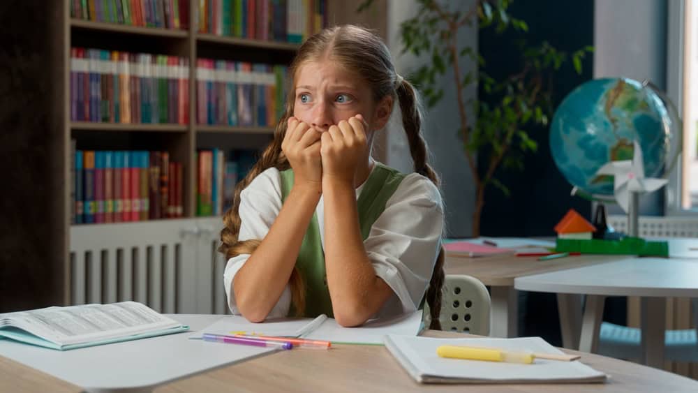Scared worried anxious Caucasian little girl fearful frightened school child kid nervous pupil schoolgirl student primary education learner biting nails afraid fail test exam worry problems classroom