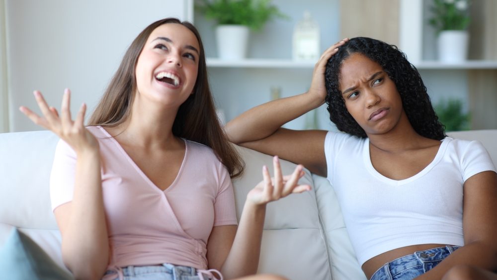 Overwhelmed black woman listening a vain friend sitting on a couch at home