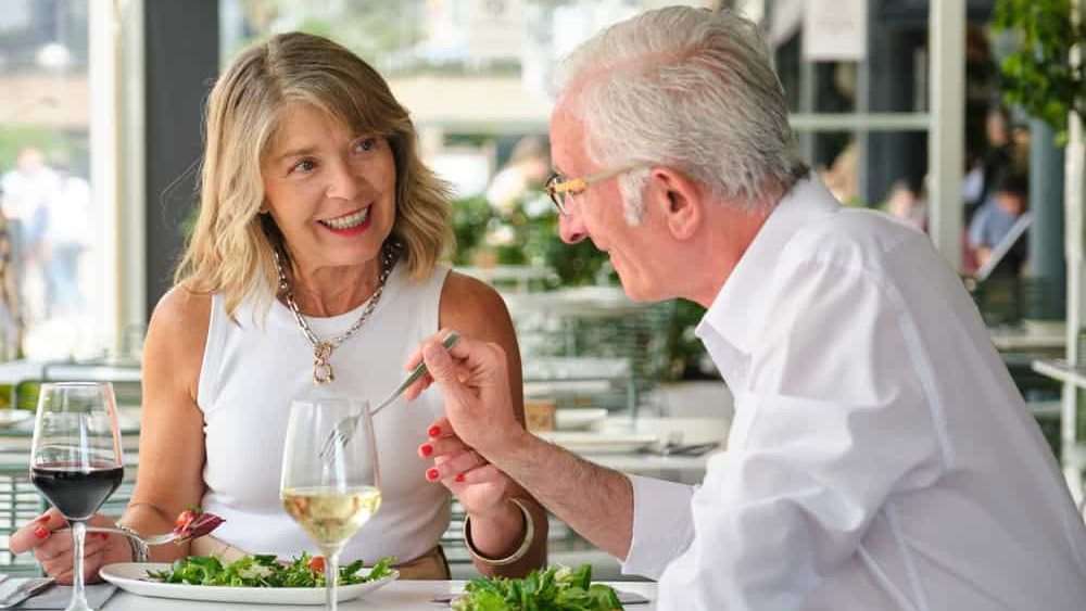 Happy mature couple eating fresh salad and drinking wine, having a pleasant conversation during their lunch date