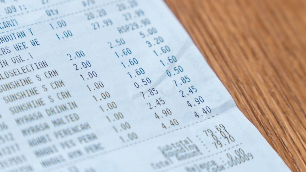 Printed grocery receipt on a wooden table. Shopping, expenses, budgeting concept.