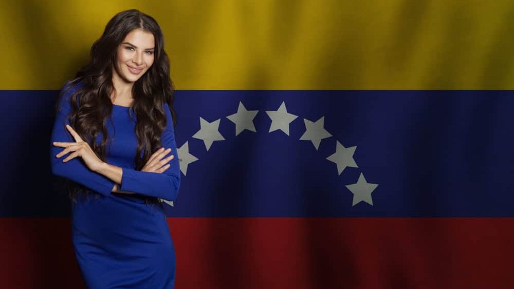Successful young woman in blue dress smiling against flag of Venezuela background