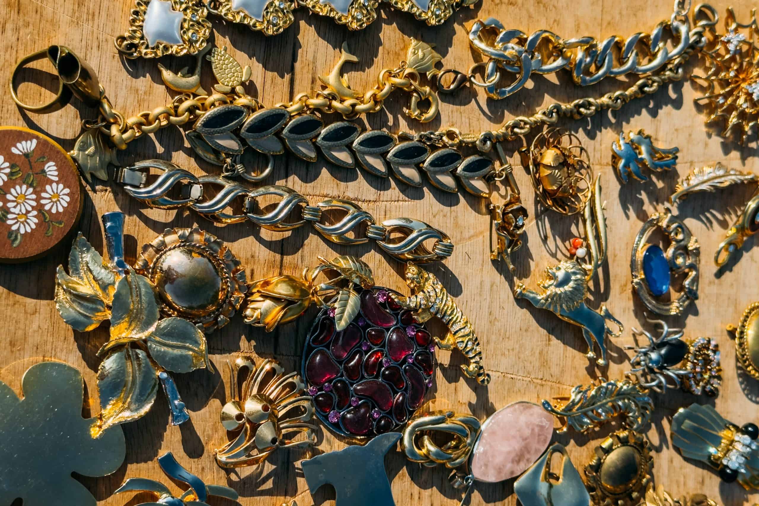 Close-up of ornate vintage gold jewelry and brooches with floral and animal motifs laid out on wood. Vintage jewelry, flea market, secondhand style, maximalist accessories