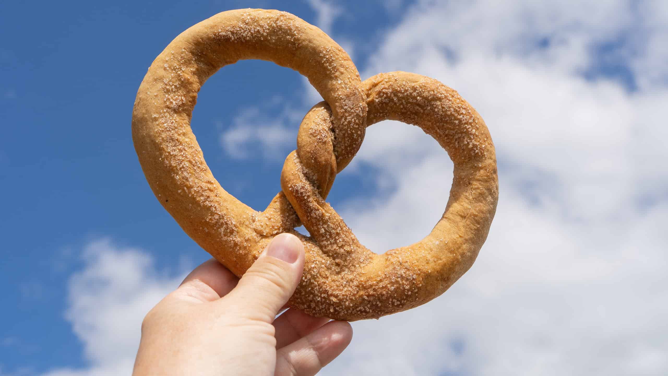 Freshly baked pretzel against blue sky. Hand hold pretzel