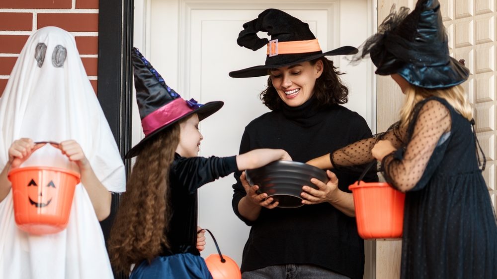 Happy people celebrating Halloween. Adult is treating with sweets children outdoors.