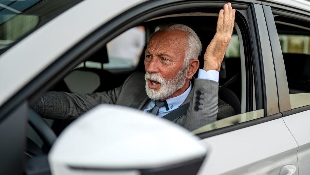 Upset mature executive having a road rage, arguing and gesturing to other drivers while driving his car