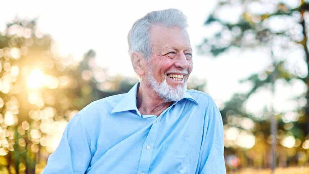 Portrait of an elderly man outdoors. Happy senior man sitting on a bench in park