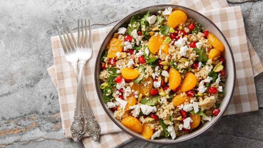 Diet quinoa salad with spinach, feta, tangerines, pomegranate, and pistachios dressed with a lemon-yogurt sauce, close-up in a bowl on a table. Horizontal top view from above