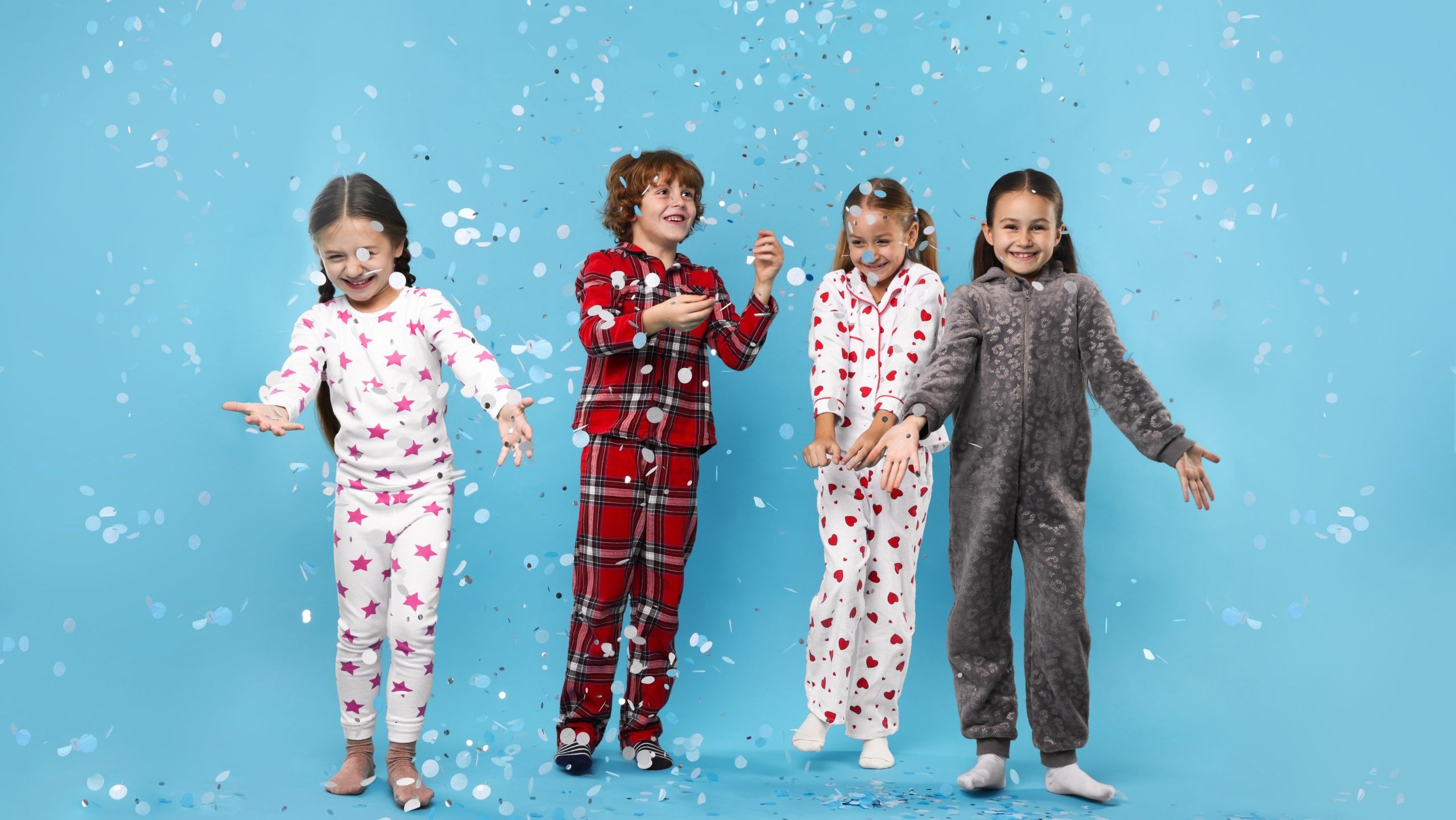 Cute children in pajamas with confetti on light blue background