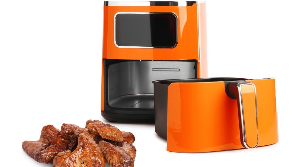 Orange air fryer and cooked chicken wings on white background