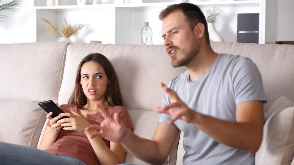 Disgusted woman listening her partner talking absurdly sitting on a couch at home