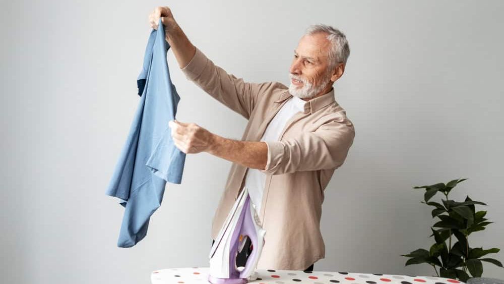 Senior man smiling, preparing to iron clothes, enjoying household chores and daily routine