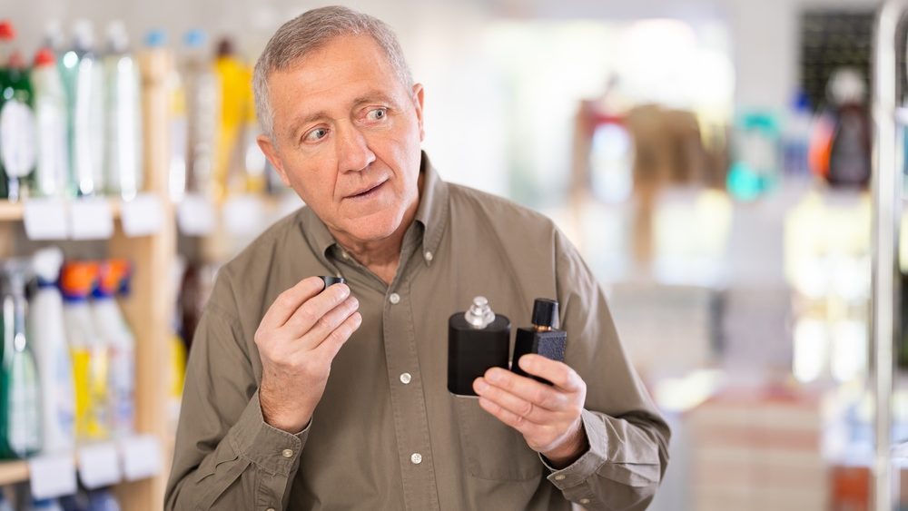Elderly man standing in a supermarket tastes perfume. Buyer came to the store for a new perfume