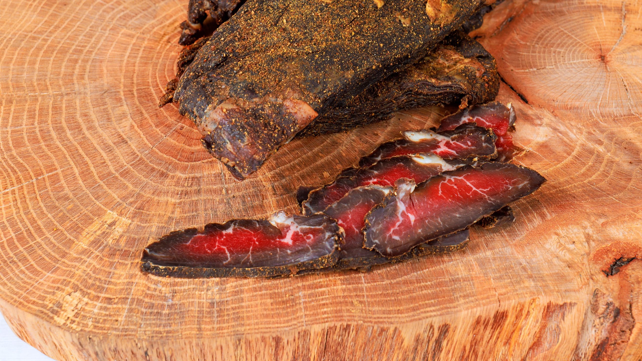 Beef jerky slices are placed on wooden board to larger piece of whole cured beef
