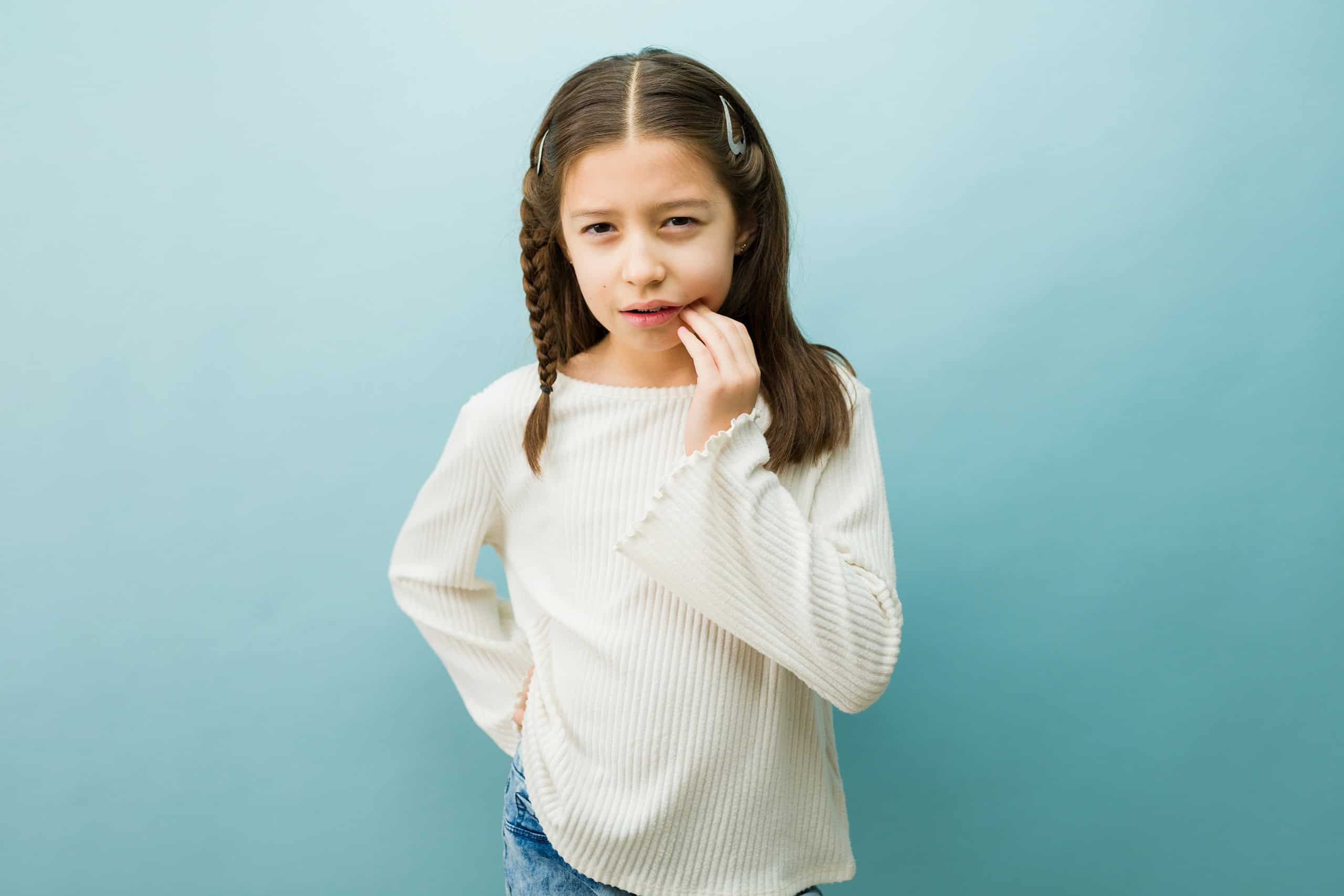 Tween girl suffering from toothache, pressing finger against her cheek, feeling pain and discomfort due to dental sensitivity