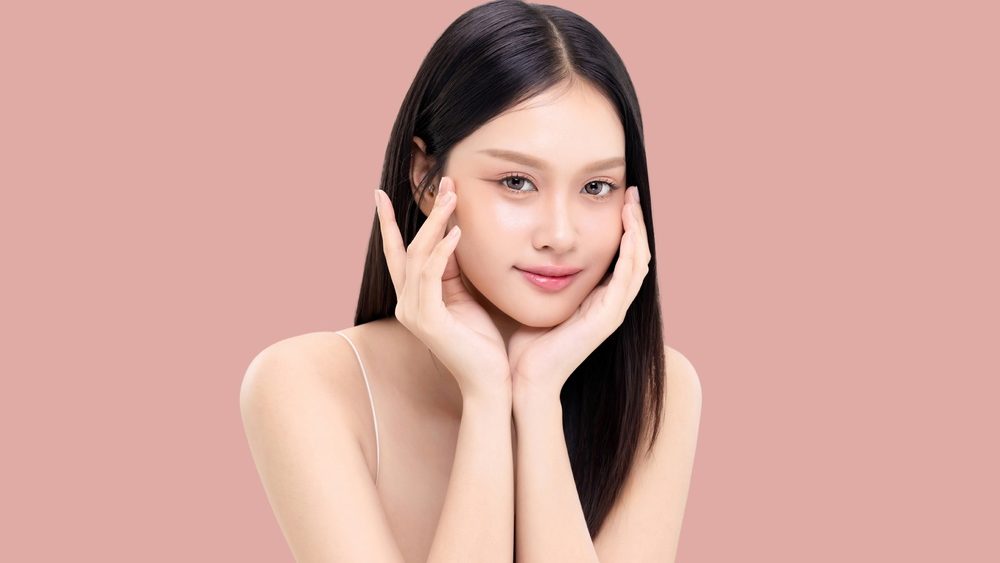 Beautiful young Asian woman with long straight hair and healthy smooth skin isolated on pink background. Ideal for use in beauty skincare commercial campaigns and wellness advertising.