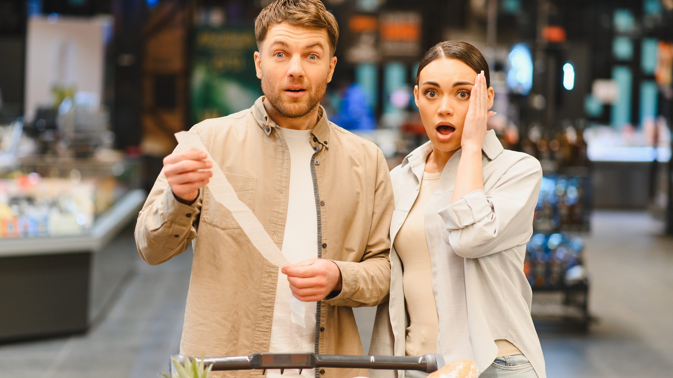 Couple looking shocked and surprised, holding a long supermarket receipt displaying high prices, experiencing inflation and financial burden