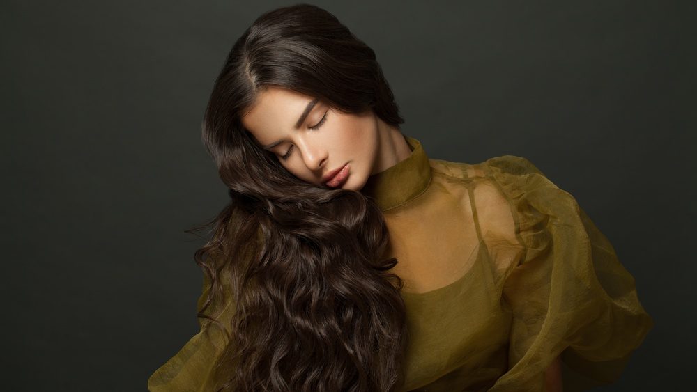 Young woman hair. Beautiful model with long curly hairstyle posing