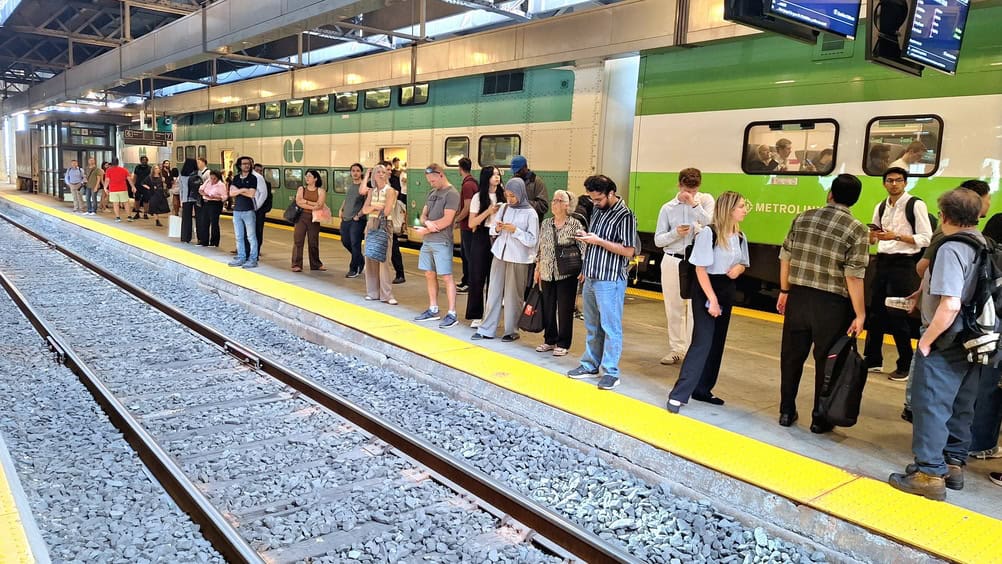 Toronto, ON, Canada - July 23, 2026: Commuters wait on a train station platform next to a green and white train in Toronto.